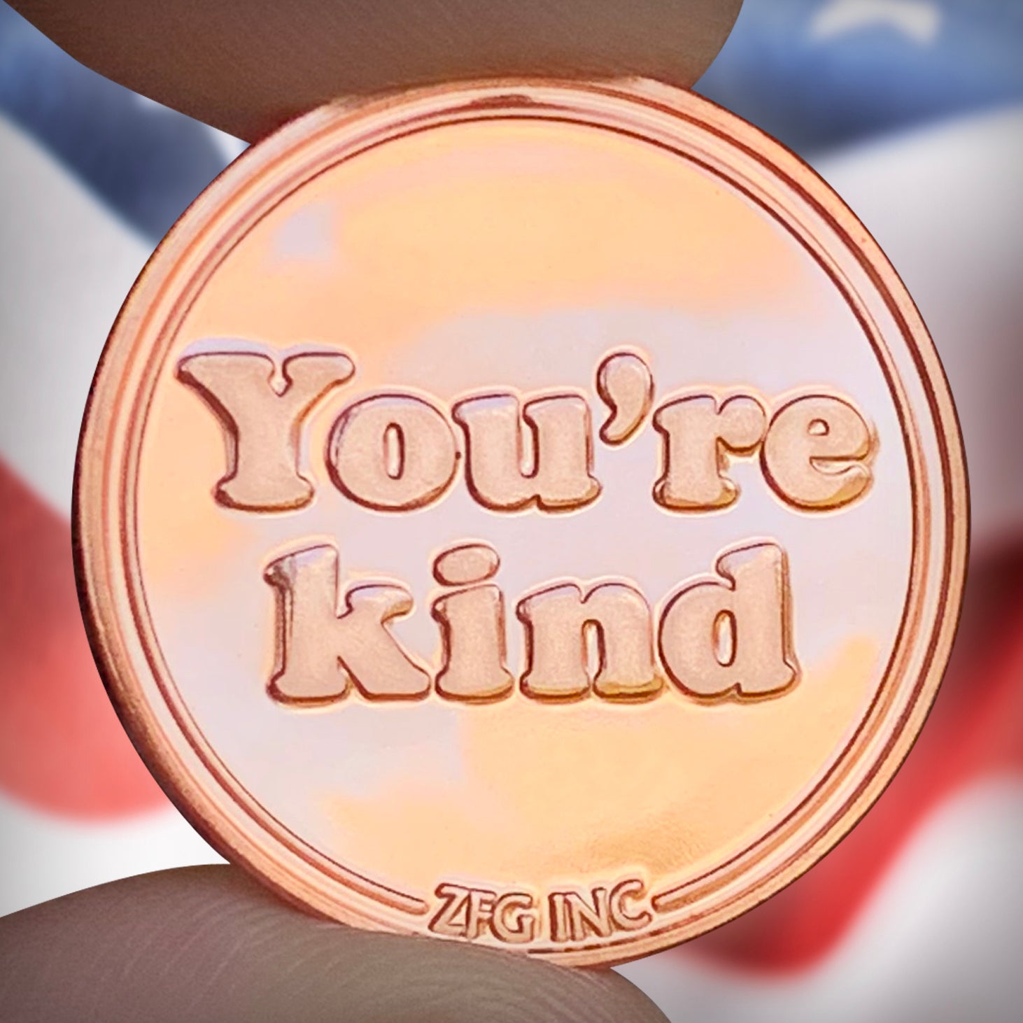 copper coin with 'You're kind' text held by a hand against a blurred background