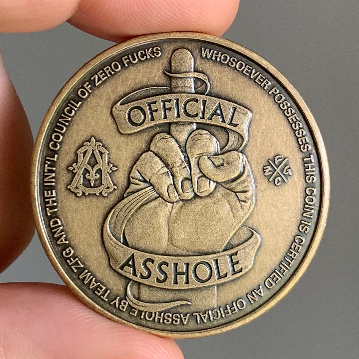 Bronze coin with text and design, held by a hand against a gray background