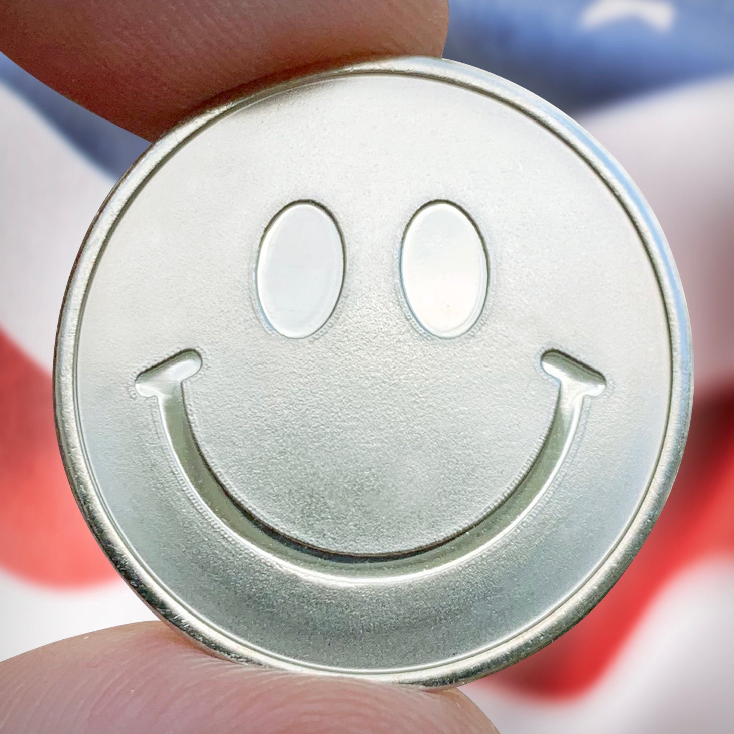 Metallic smiley face coin held between fingers 