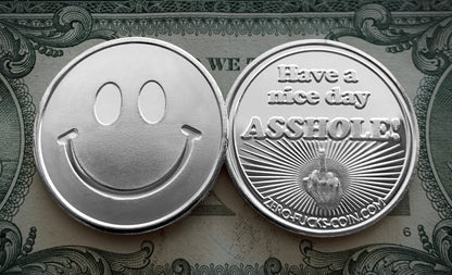 Two silver coins with one displaying a smiley face and the other with a rude message on a dollar bill background.