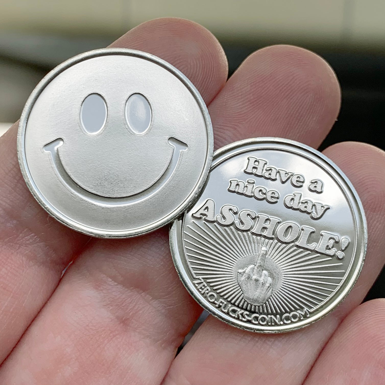 Two coins, one with a smiley face and the other with a humorous message, held in a hand.